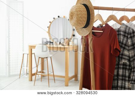 Hangers With Stylish Clothes And Hat On Rack In Makeup Room. Space For Text