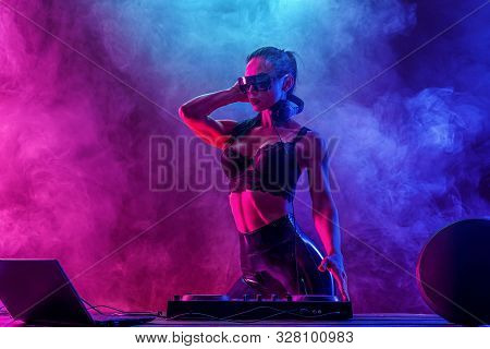 Young Sexy Woman Dj In Bra And Sunglasses Playing Music. Headphones And Dj Mixer On Table. Colorful 
