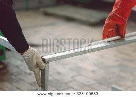 Workers Measure The Length Of The Iron Frame With A Tape Measure.
