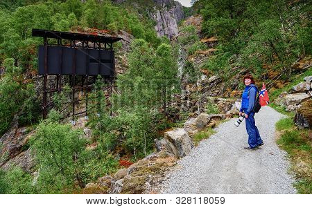 Tourist Woman With Norwegian Flag And Camera Walking Trough Mountains Path In Allmannajuvet Area Sau