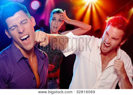 Dva mladí muži bopping v nočním klubu pro ženu, která se dívá ustaraně na pozadí.