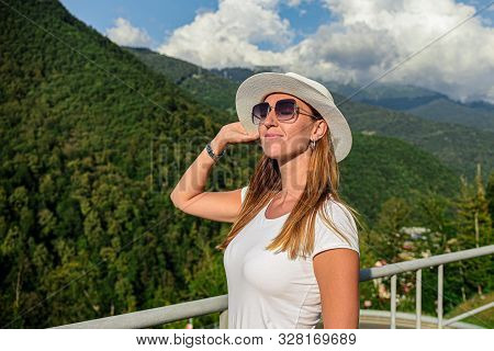 A Girl In A White T-shirt Wearing Sunglasses And A White Hat In The Mountains Admiring The View