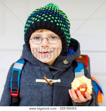 Little Kid Boy With Eye Glasses On The Way To The School And Eating Fresh Apple. Child With Missing 