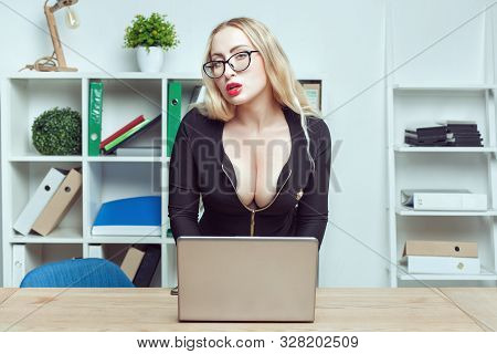 Portrait Of A Beautiful Woman Secretary In Office. She Looks With A Languid Look And Types On A Lapt