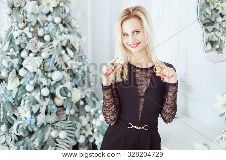 Cute Blonde Woman Stands Near A New Year Tree And Holds Bitcoin Coins In Her Hands.