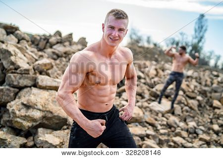 Two Fitness Strongmen Having Workout Outdoor In A Rocky Background. Bodybuilders Concept Background 