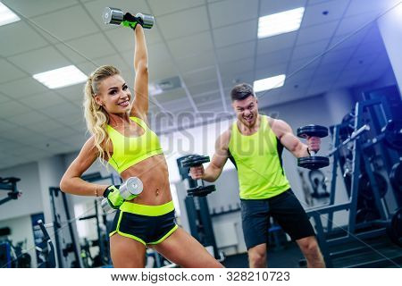 Gorgeous Blonde Woman Is Warming Up With Dumbbells And Doing Workout At A Gym Looking In The Camera.
