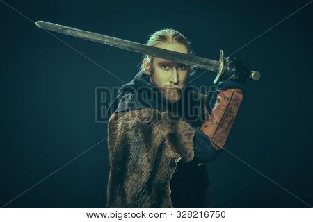 Portrait of a medieval knight in armour and with a sword over black background. Historical reenactment.