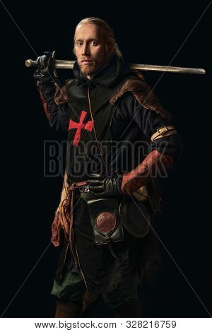 Portrait of a medieval knight in armour and with a sword over black background. Knight Templar. Historical reenactment.