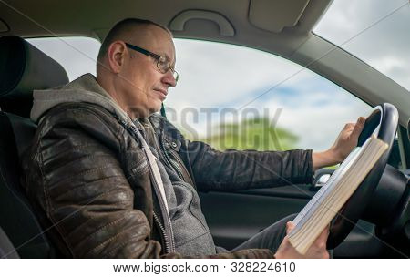 A Man Is Reading A Book While Driving A Car And Is Distracted