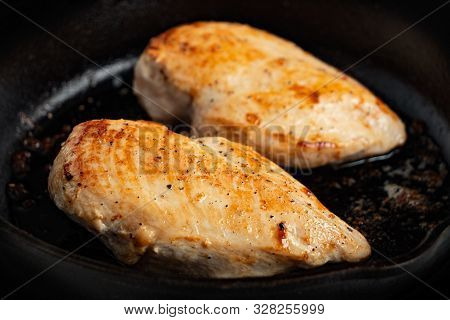 Closeup Of Two Whole Chicken Breasts Roasting In Cast Iron Pan.