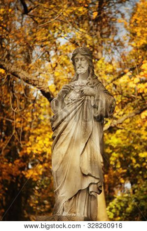 Anient Statue If Jesus Christ Against A Background Of Golden Autumn Leaves In The Sun's Rays