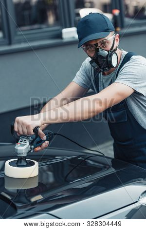 Car Cleaner In Respirator And Protective Glasses Looking At Camera While Polishing Car With Polish M