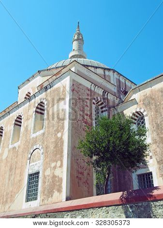 The Suleiman Mosque In Rhodes Old Town With Dome And Tall Minaret Against A Blue Sunlit Sky