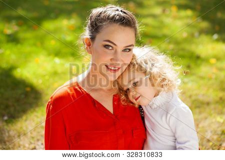 Closeup portrait of a young beautiful brunette woman with little curly daughter in autumn park