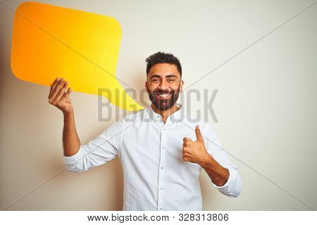 Young arab indian hispanic man holding speech bubble over isolated white background happy with big smile doing ok sign, thumb up with fingers, excellent sign