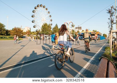 Novosibirsk, Russia - 08.25.2019: Couple On Bikes Rides Against Two Large Ferris Wheels In The Park 