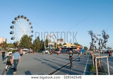 Novosibirsk, Russia - 08.25.2019: Scooters And Skaters Against Two Large Ferris Wheels In The Park O