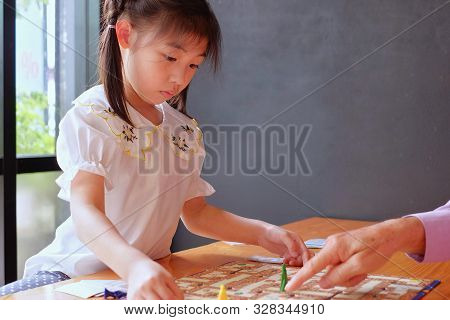 A Cute Asian Preschool Girl Learning To Play Board Games With Her Grandfather