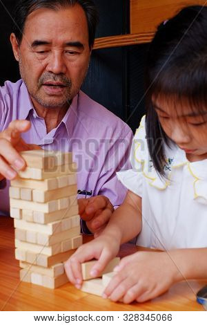 An Grandfather Is Teaching His Granddaughter To Play A Block Wood Tower Game.