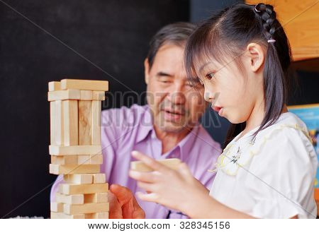 An Grandfather Is Teaching His Granddaughter To Play A Block Wood Tower Game.