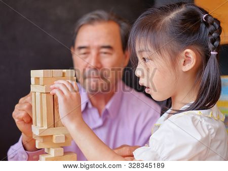 An Grandfather Is Teaching His Granddaughter To Play A Block Wood Tower Game.