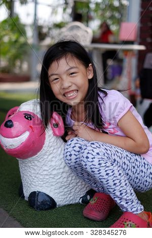 An Young Attractive Asian Girl Posing Next To A Painted Cray Sheep, Smiling.