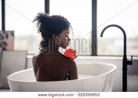 Curly Dark-skinned Woman Holding Loofah While Having Bath