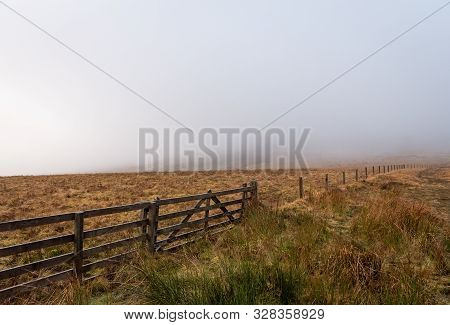 A Wooden Fence That Stretches Between Scotland And England Border With Brown Grass Field On Either S