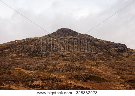 A Hill In The Scottish Highlands Covered In Brown Wintery Grass On A Cloudy And Grey Day.