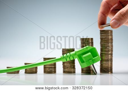 Hand Stacking Coin On Energy Prices Chart Near Ac Power Plug