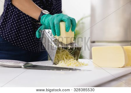 Woman With Green Gloves Grating Cheese On Kitchen Table.