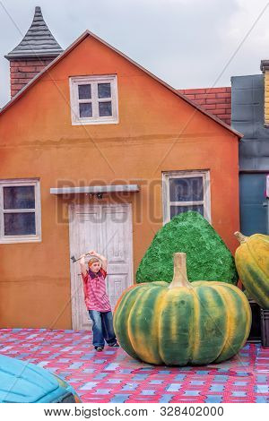Funny Picture Of A Lilliput Toy Boy Is Cutting A Pumpkin By An Axe.