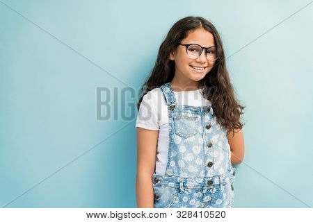 Portrait Of Smiling Preadolescent Girl Wearing Denim Overalls While Standing Against Turquoise Backg