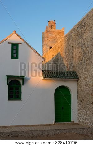 Entrance of a traditional house near the fortification wall and tower in twilight in the medina of Asilah, Morocco