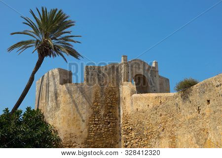 Outside of the old stone fortification wall and gate of Asilah, Morocco with a blue sky