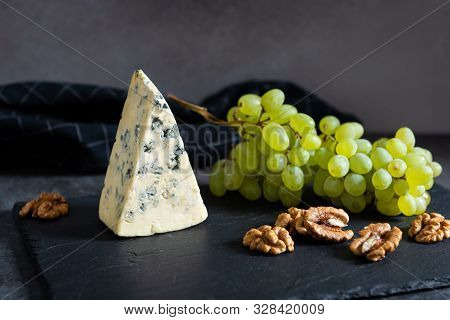 Tasty Blue Cheese Served With Green Grapes And Walnuts On A Black Stone Board. Dorblu Cheese Pieces.