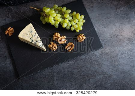 Tasty Blue Cheese Served With Green Grapes And Walnuts On A Black Stone Board. Dorblu Cheese Pieces.