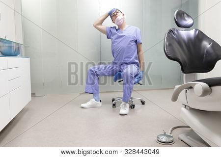 Caucasian male dentist stretching his  neck in the office during break
