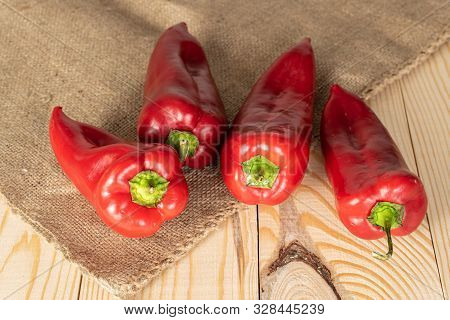 Group Of Four Whole Sweet Red Bell Pepper On Jute Cloth On Natural Wood