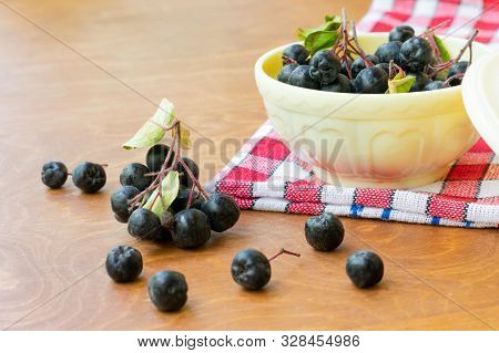 Ripe Black Chokeberries (aronia Melanocarpa) In A White Bowl On Red Napkin On Wooden Table. Bowl Ful