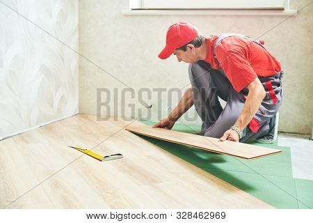 worker laying laminate floor covering at home renovation