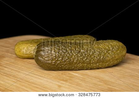 Group Of Two Whole Sour Green Pickle Front Focus On Bamboo Cutting Board Isolated On Black Glass