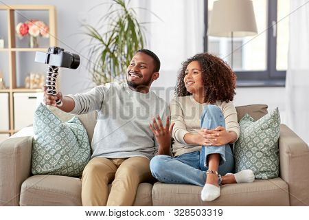 blogging, videoblog and people concept - happy african american couple of video bloggers with camera videoblogging at home