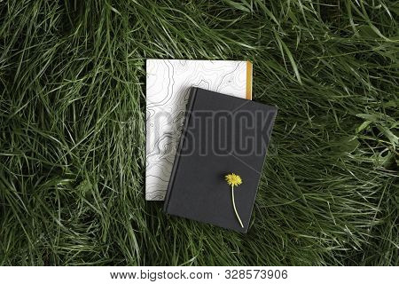 Black Book And Notebook Lie On The Grass, Background. Layout Notebook And Book. White Notebook With 