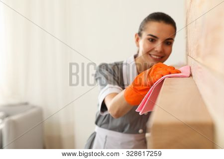 Young Chambermaid Wiping Dust From Furniture With Rag In Hotel Room, Closeup. Space For Text