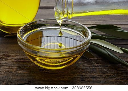 Bottle Pouring Olive Oil In A Bowl On Vintage Wooden Background