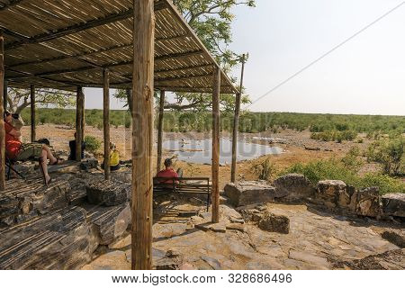 Halali, Namibia - April 3, 2019 : Tourists Wait For Wildlife Sitting On A Bench At The Moringa Water