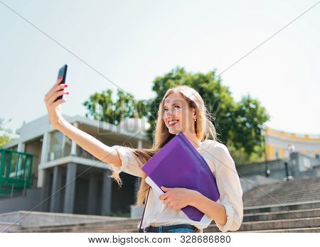Young Caucasian Woman Student In Casual Clothing With Esse In Folder Doing Selfie On Phone Going Dow