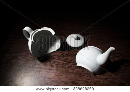 Broken Teapot On A Dark Toned Foggy Background. Pieces Of Ceramic Teapot On Wooden Table.